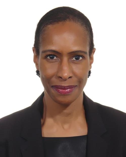 Ann Simmons smiling, with very short hair, red lipstick, earrings and a black jacket over a black top.