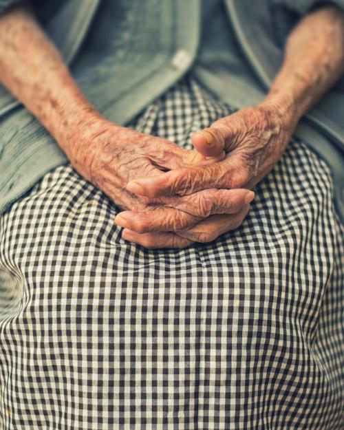 Hands of an elderly person clasped on a gingham print skirt